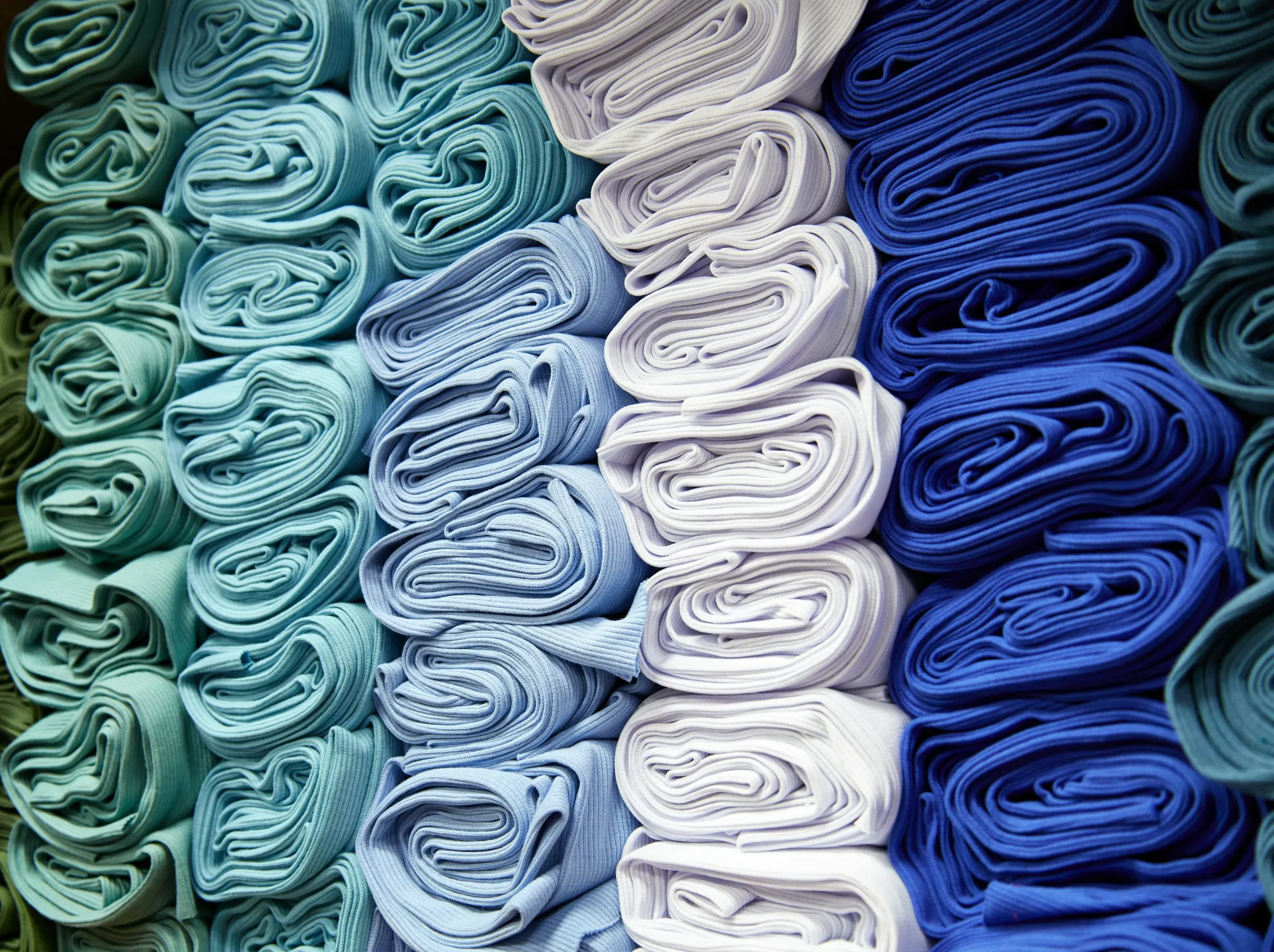 Rolos de malha em tons de azul, branco e verde-água empilhados